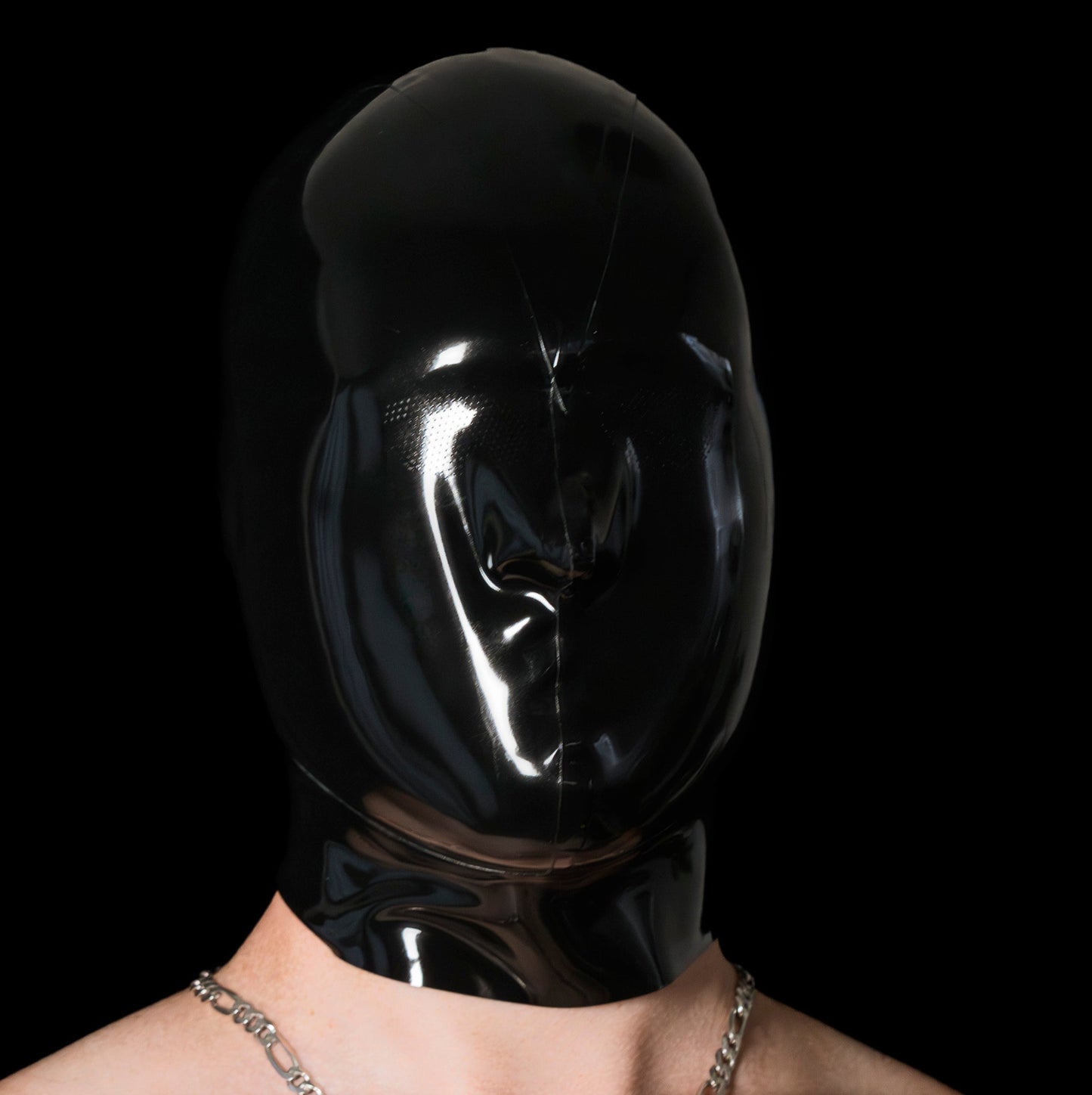 Person wearing a black latex hood with a dark background